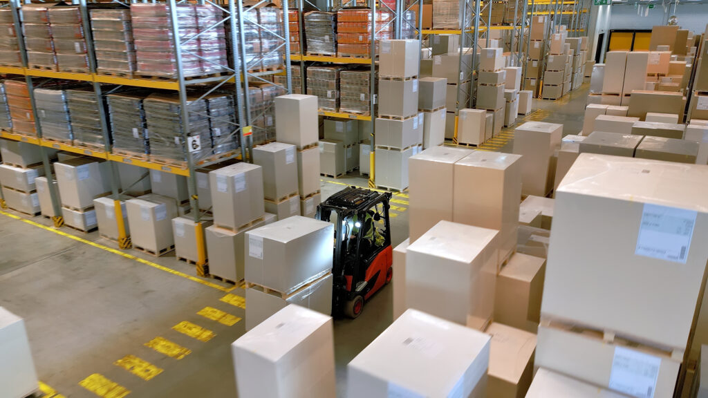 A forklift navigates a warehouse, highlighting the global supply chain's efficiency and logistics' precision. The aerial view showcases the organized chaos of stacked boxes and crates.